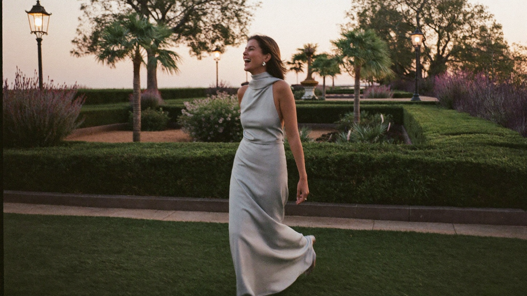 Woman in an elegant maxi dress walking through a garden courtyard at sunset